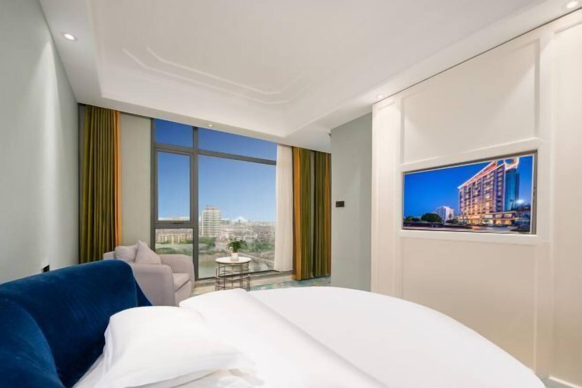 Ein Hotelzimmer mit großem Fenster, einem Bett, einem kleinen Tisch und Blick auf die Stadt.