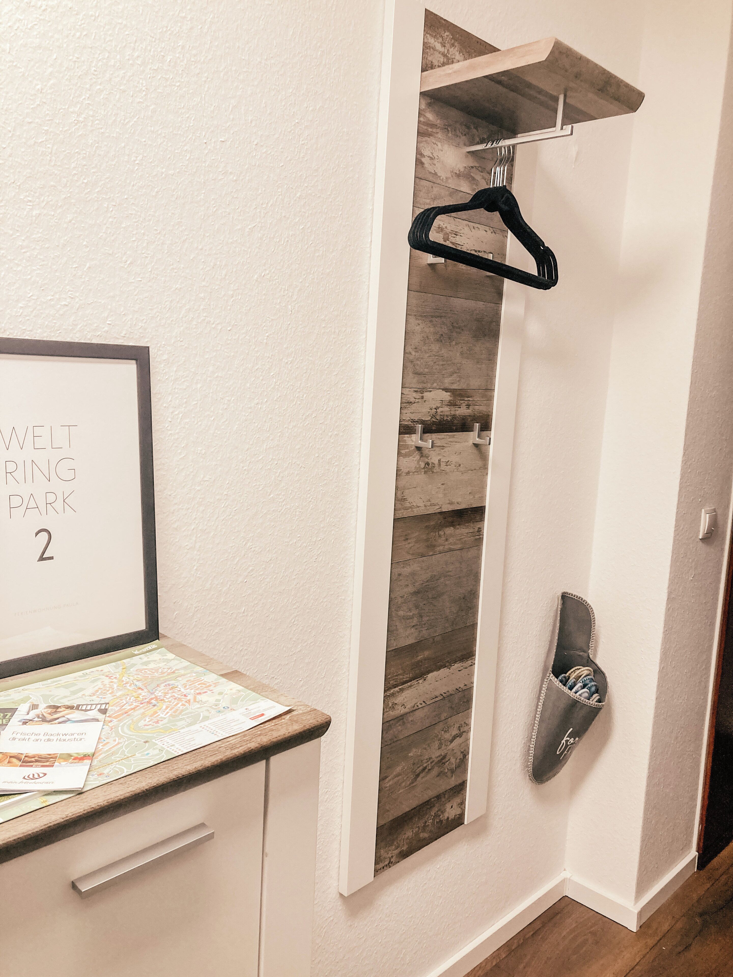 A hallway with a framed sign reading "WELT PARK 2", a shoe rack, and a wooden wall panel.