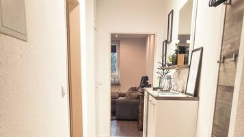 A narrow hallway with wooden flooring, a patterned rug, and a door leading to a living area with a sofa and a coffee table.