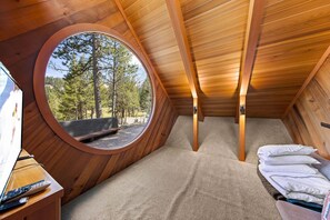 A cozy room with a circular window, a bed, and a TV on a wooden stand.