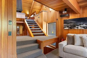 A wooden interior with a staircase, a couch, and a painting.