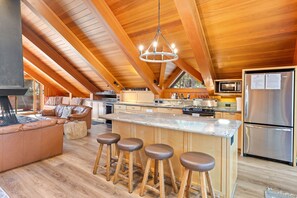 A spacious kitchen with a central island, wooden ceiling beams, and a stainless steel refrigerator.