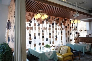 Un restaurante con techo de madera, luces colgantes, un sofá amarillo y una mesa con mantel verde.