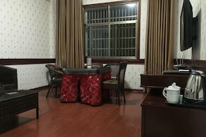 A room with a dining table, chairs, a TV, a coffee maker, and a window with curtains.