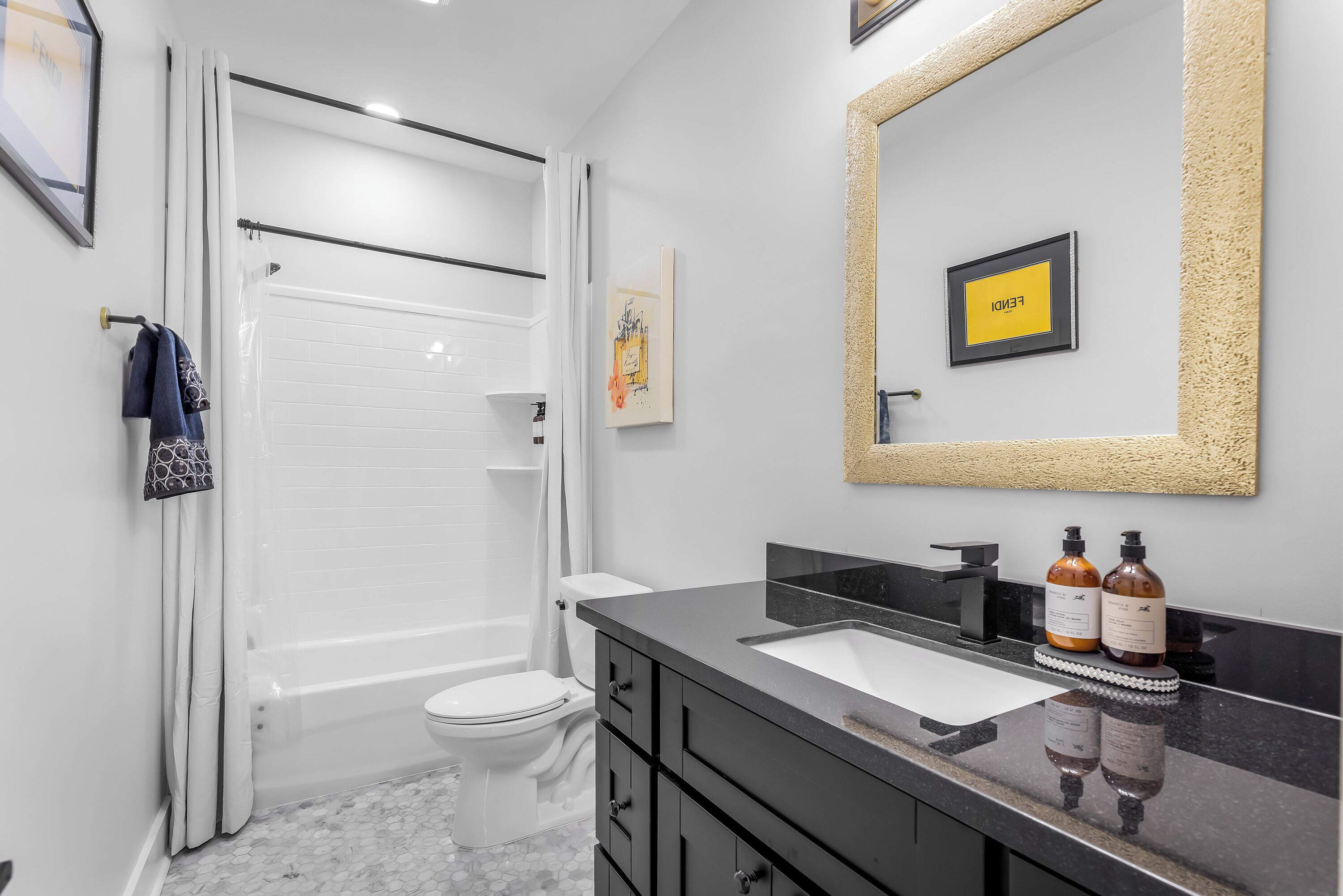 A modern bathroom with a bathtub, toilet, and a vanity with a sink and two bottles of shampoo.