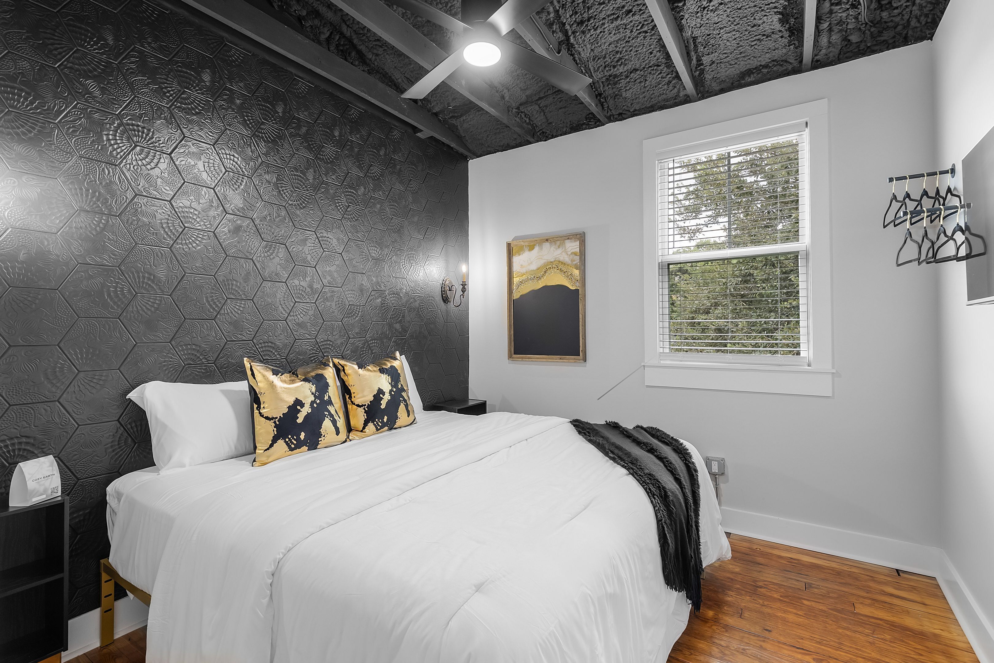 A bedroom with a bed, a nightstand, a window with blinds, and a wall-mounted coat rack.