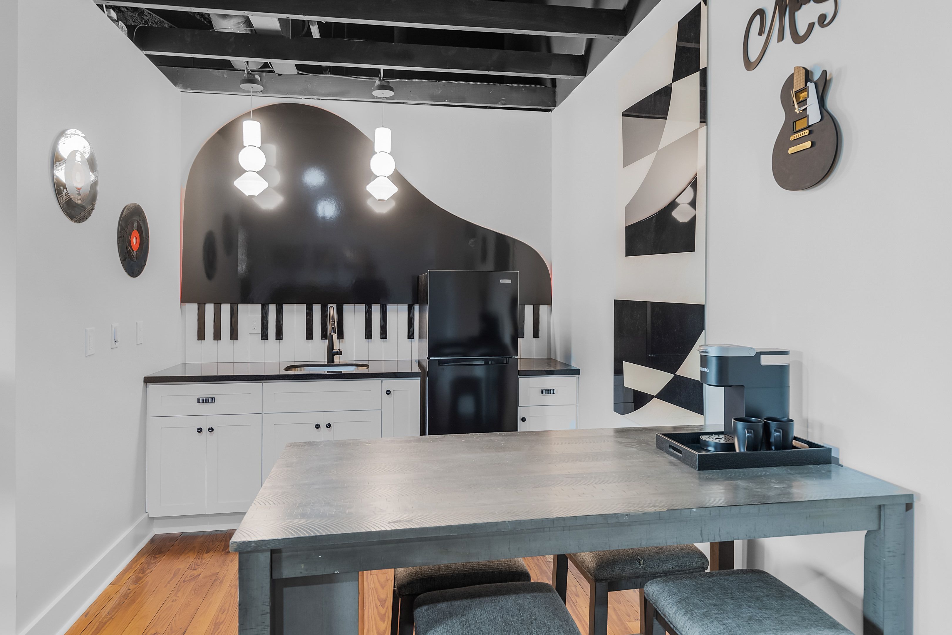 A modern kitchen with white cabinets, a black refrigerator, and a piano-shaped light fixture.