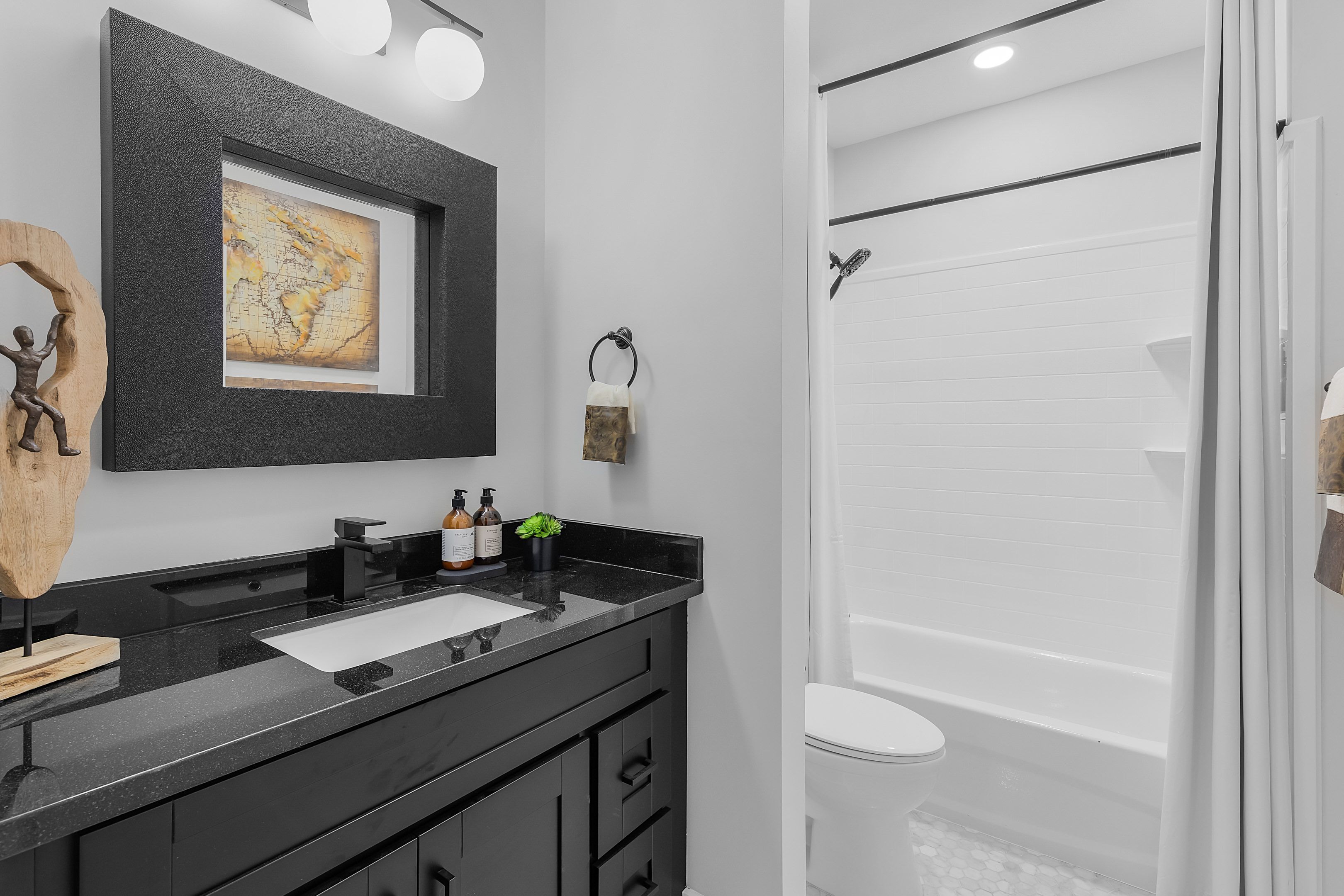 A modern bathroom with a black vanity, a framed map, a wooden sculpture, and a white bathtub.