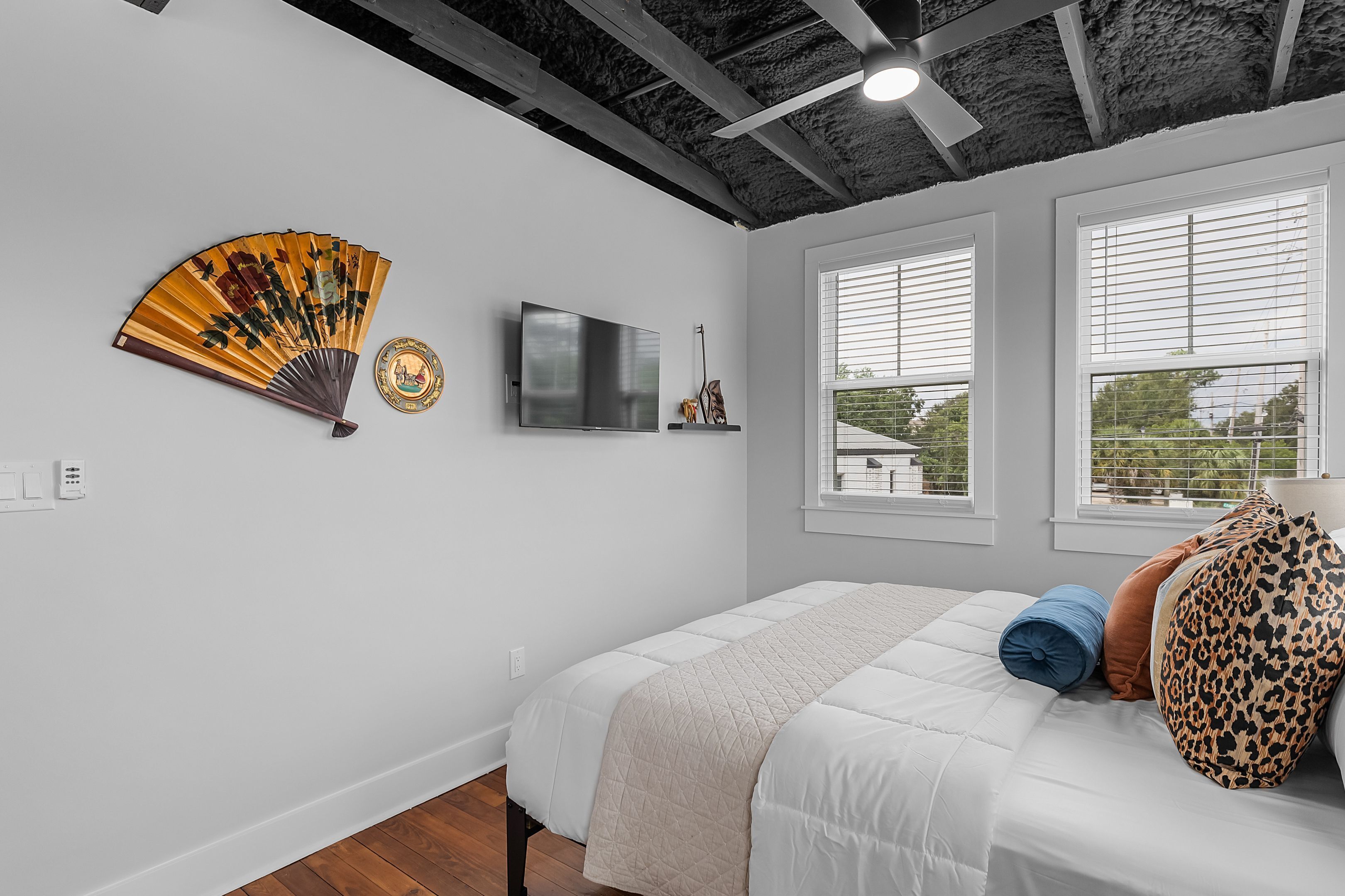 Une chambre à coucher avec un lit, un ventilateur, une télévision et des fenêtres.