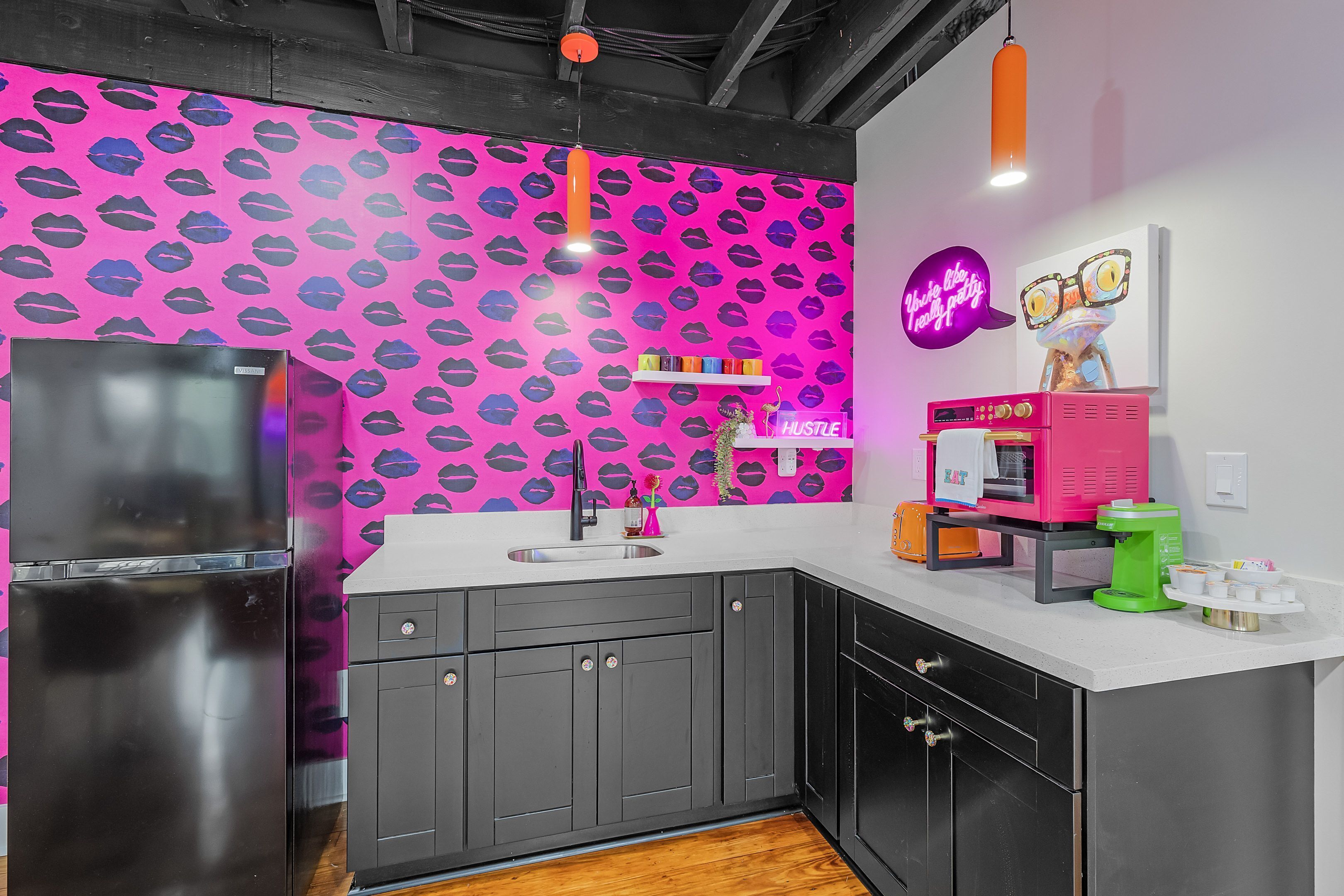 A kitchen with a pink wall, black cabinets, and a white countertop.