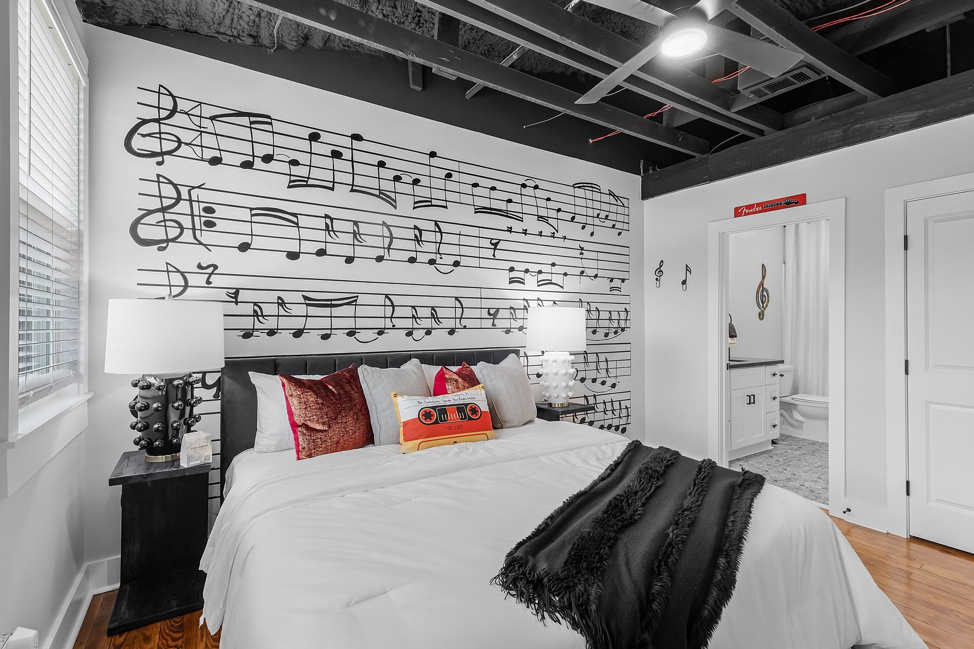 A bedroom with a bed, white bedding, a headboard with a music-themed wall, a bedside table with a lamp, and a door labeled "Premium Room."