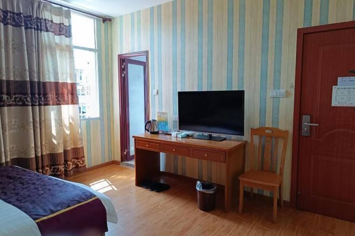 Habitación de hotel con cama, escritorio con televisor, silla, cesto de basura y puerta con un aviso.