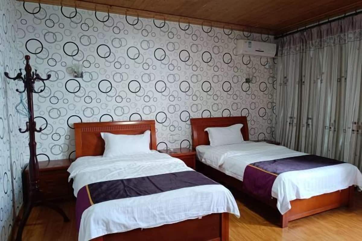 Una habitación con dos camas de madera, suelo de madera, papel tapiz estampado y un ventilador de techo.