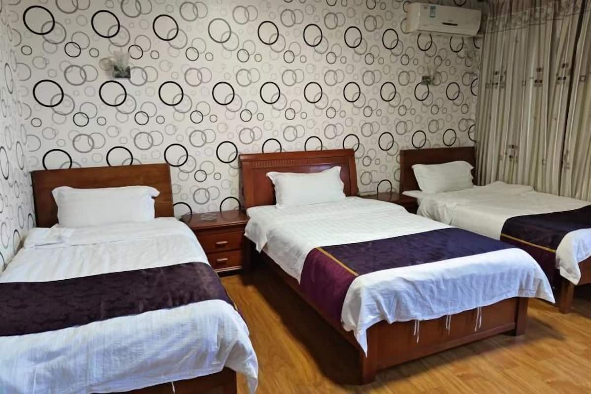 Habitación de hotel con tres camas, cabeceros de madera y un papel tapiz estampado.