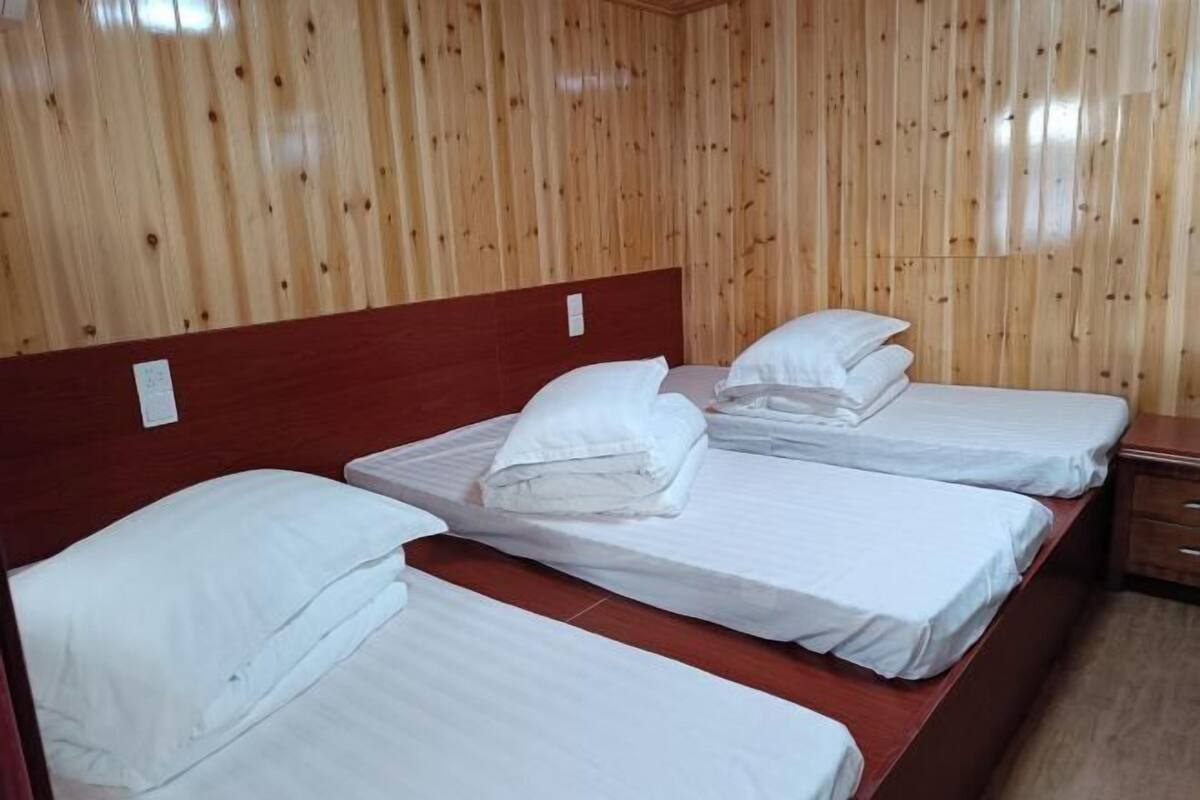 Una habitación con tres camas, paredes de madera y cabecero de madera.