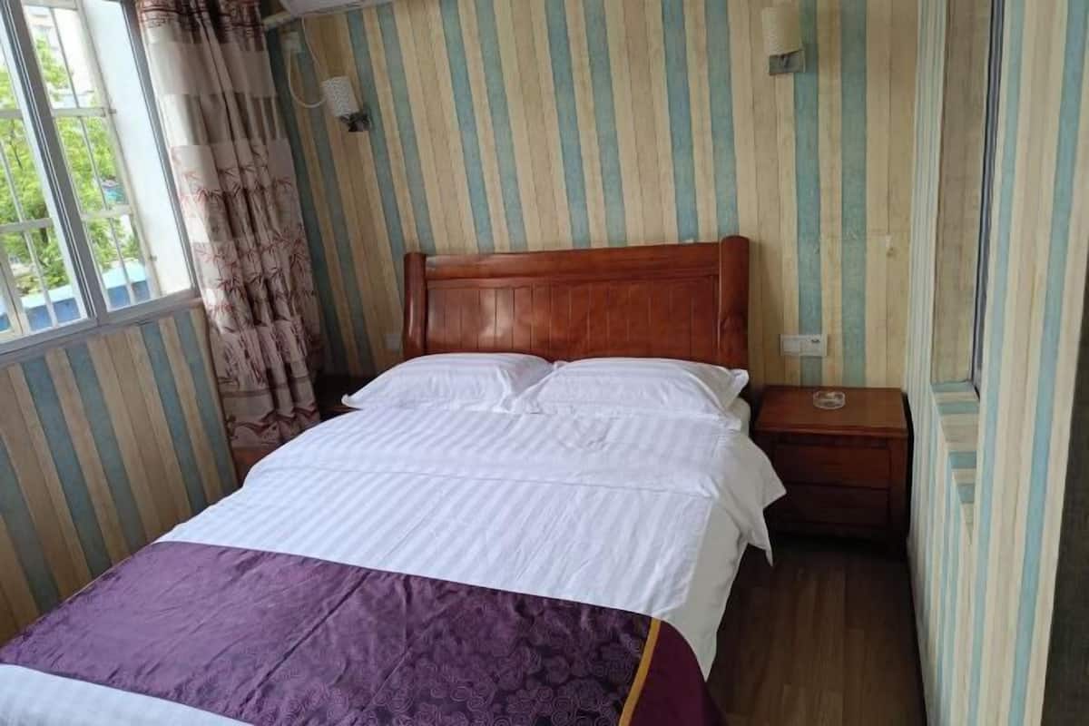 Una cama individual con cabecera de madera, una mesita de noche y una ventana con cortinas.