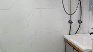 Bany amb rajoles de marbre blanc, un lavabo blanc i una dutxa amb dues mànegues.