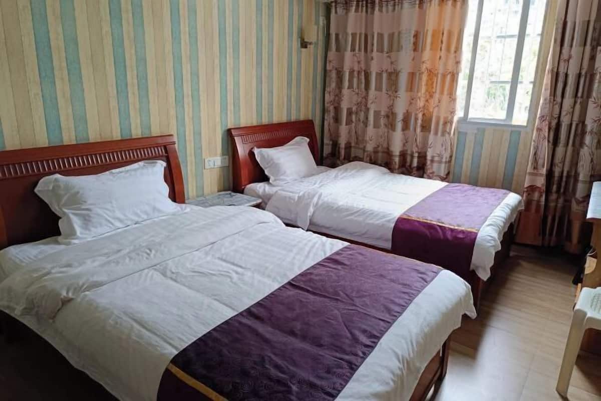 Una habitación con dos camas, paredes a rayas y un ventanal con cortinas.