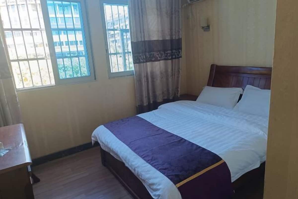 Un dormitorio con cama, mesita de noche y ventana con cortinas.