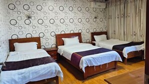 Una habitació amb tres llits de fusta, cadascun amb roba de llit blanca i una manta de llavors morada. L'habitació té un paper pintat i un sostre de fusta.