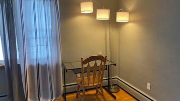 A room with a wooden chair, a glass table, and a floor lamp against a grey wall.