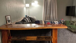 Una mesa de comedor de madera con bancos, un sofá gris, un televisor y un cuadro en la pared.