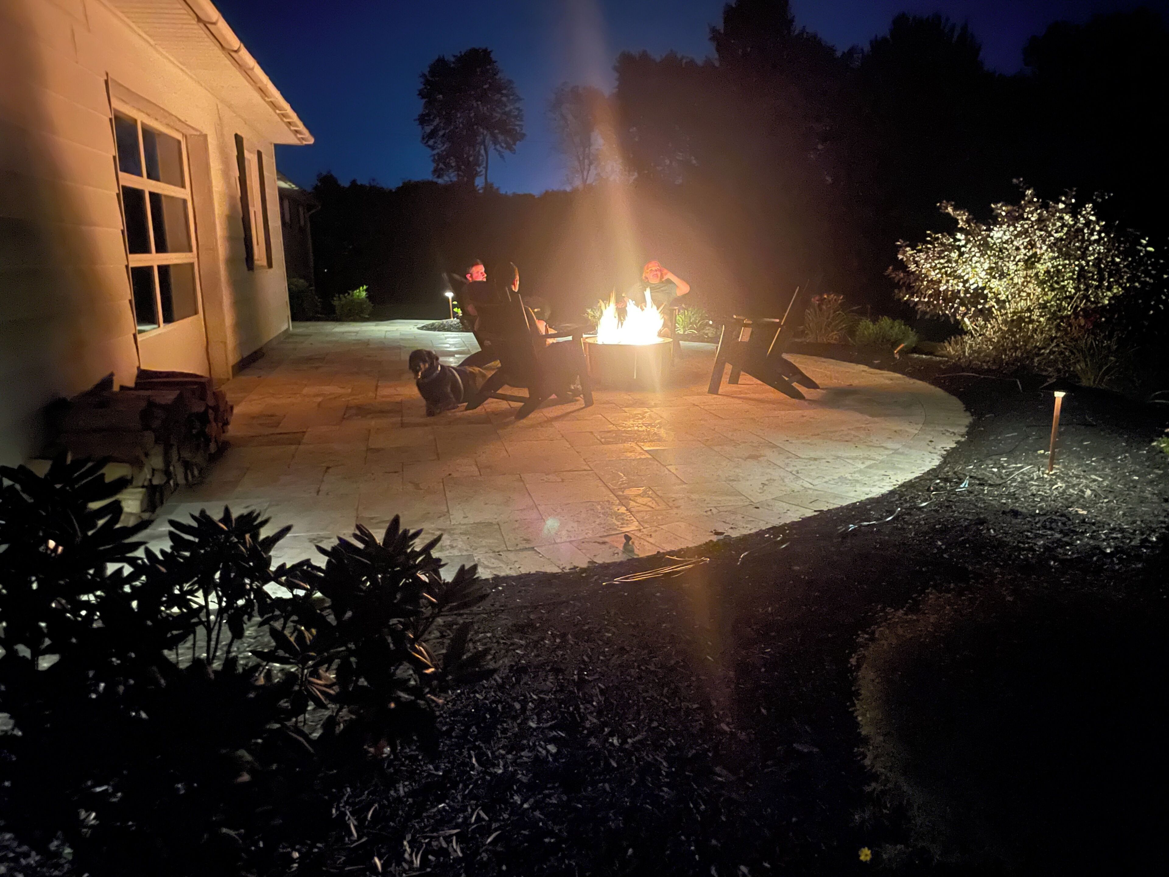 A patio with a fire pit, outdoor furniture, and a dog.