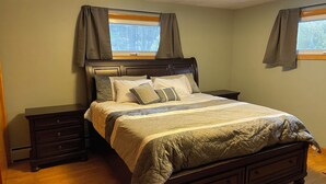 Un dormitorio con una cama grande, dos mesitas de noche, un aparador y una ventana con cortinas.