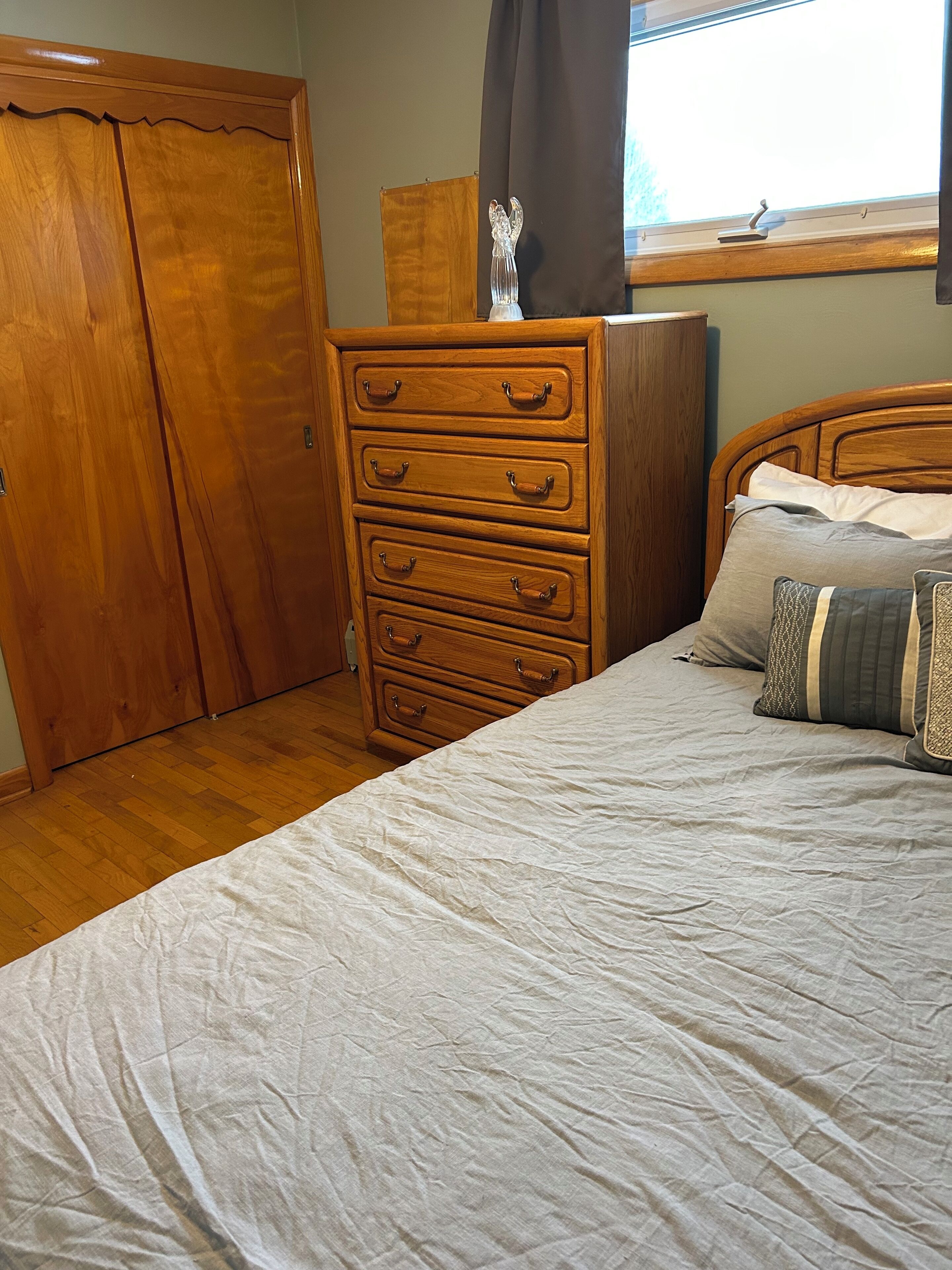 A bedroom with a wooden dresser, a bed with pillows, and a window with curtains.