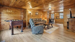 Accogliente interno di una baita in legno con un tavolo da calcio, una poltrona in pelle, un tavolo da pranzo e pensili in legno.