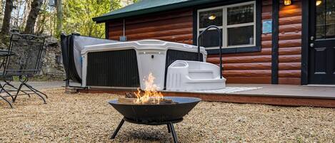Une cabane en bois, avec un foyer au premier plan et un jacuzzi extérieur abrité à l’arrière-plan.