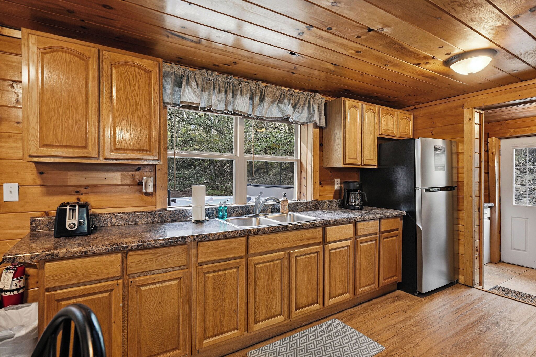 Cocina de cabaña de madera con encimera de granito, refrigerador de acero inoxidable y armarios de madera.