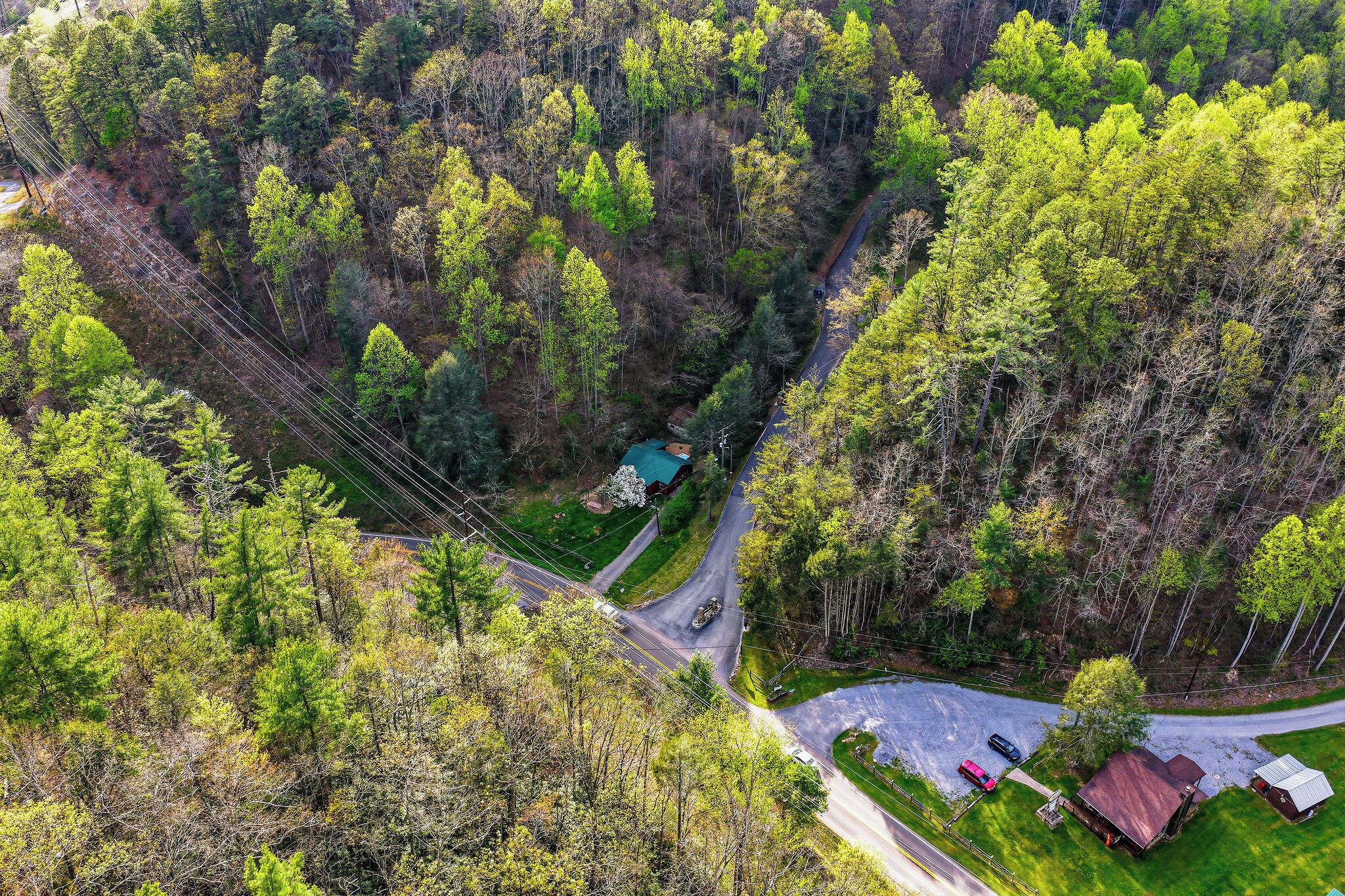 Une vue aérienne d’une zone boisée, avec une route sinueuse, un petit bâtiment et quelques véhicules.