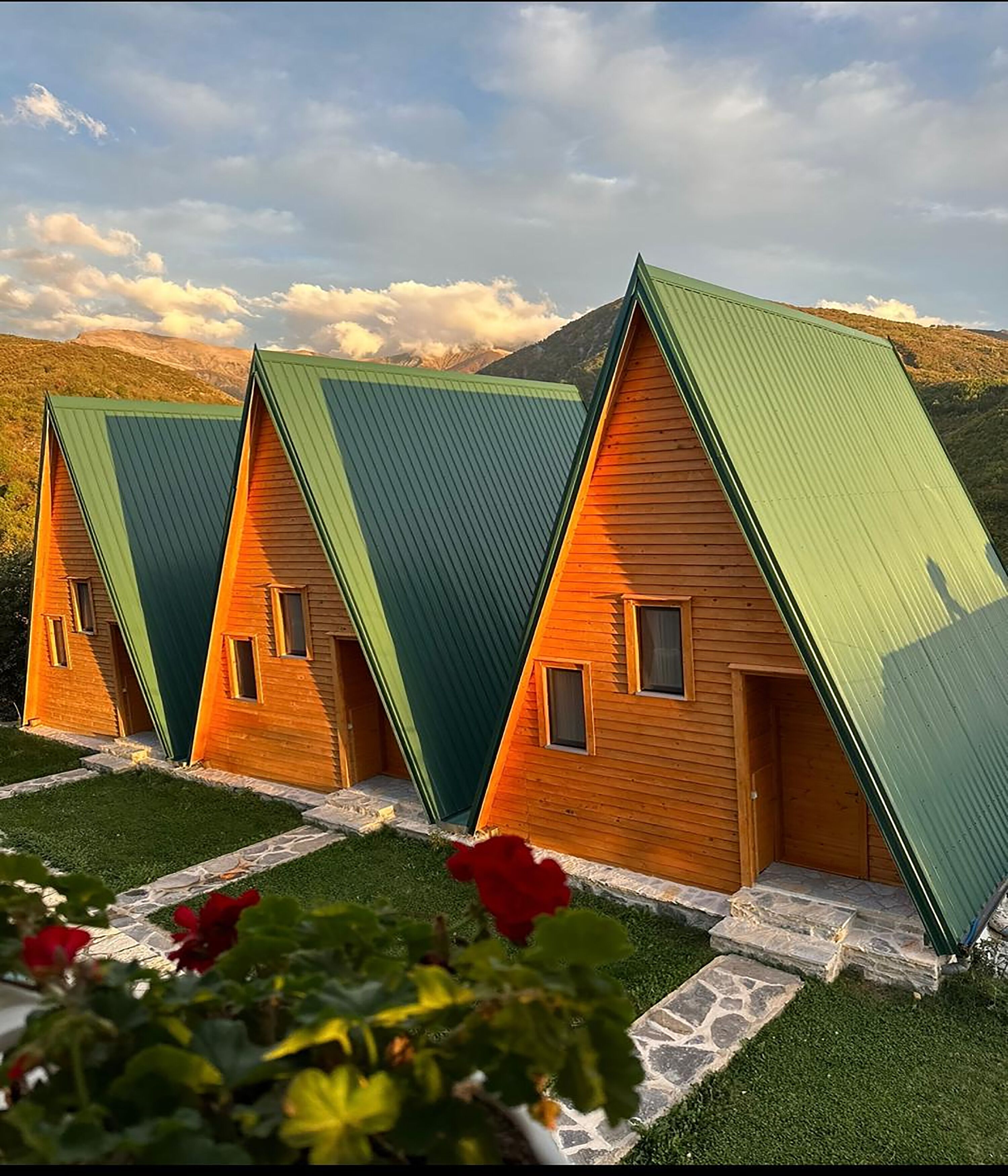 A row of wooden cabins with green roofs and stone steps leading to the entrance.