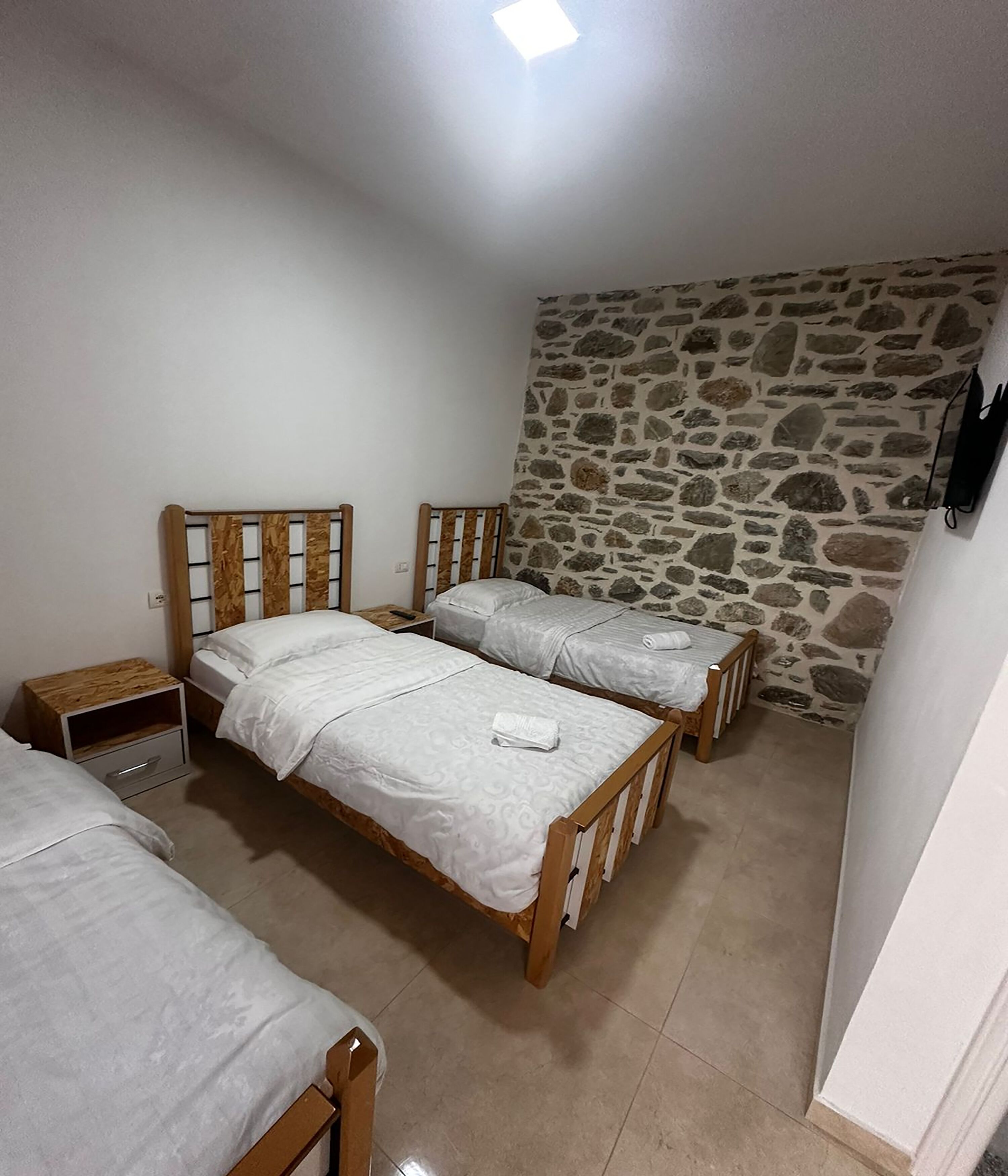 Une chambre avec deux lits en bois, un mur en pierre et une petite table de chevet en bois.