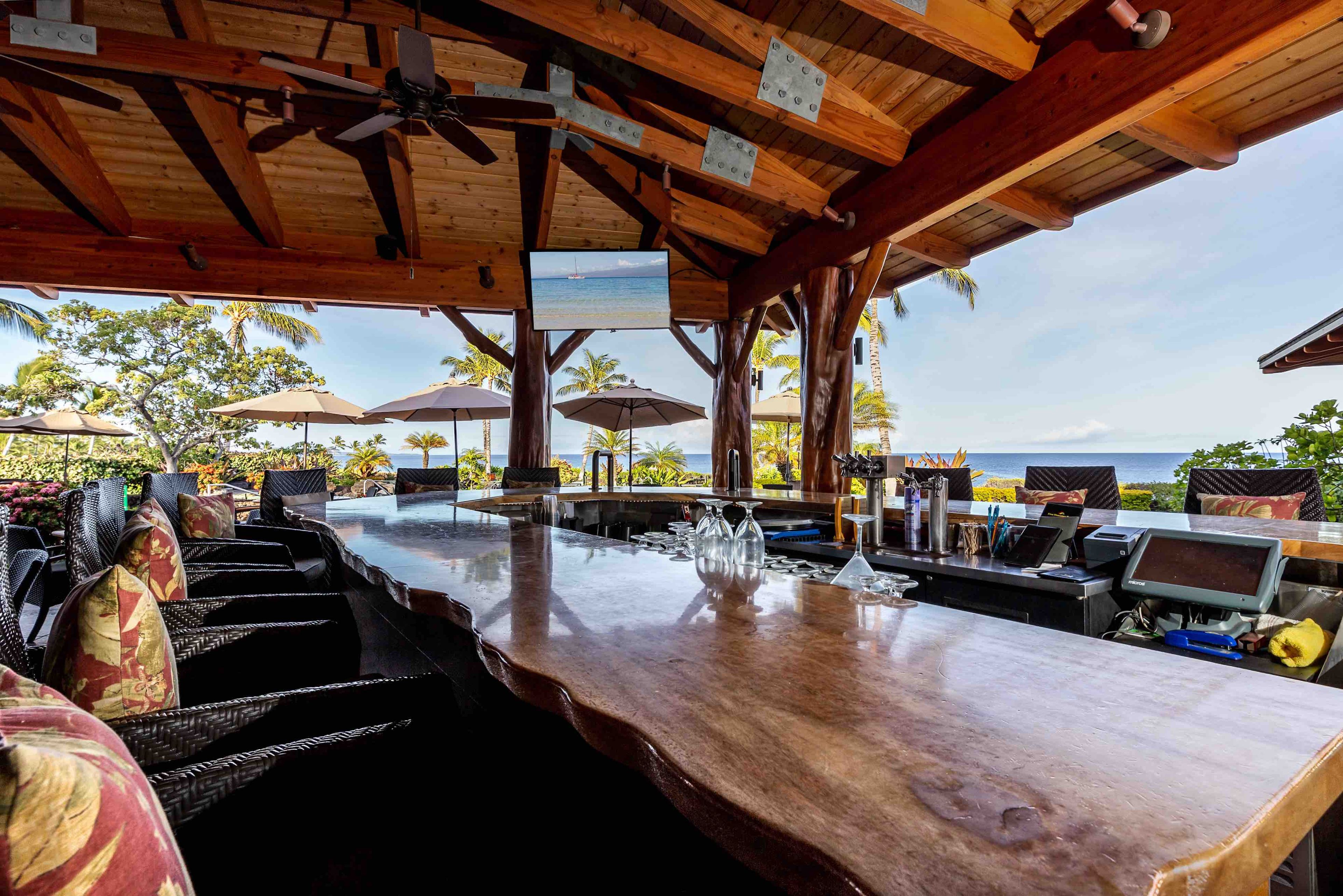 Un espace bar extérieur abrité, doté de poutres en bois, d’une table de billard et de sièges extérieurs protégés par des parasols.