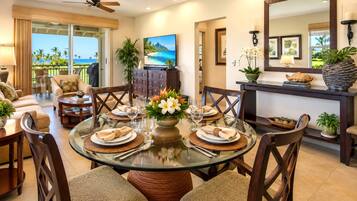 A dining area with a glass table, chairs, and a view of the ocean through large windows.