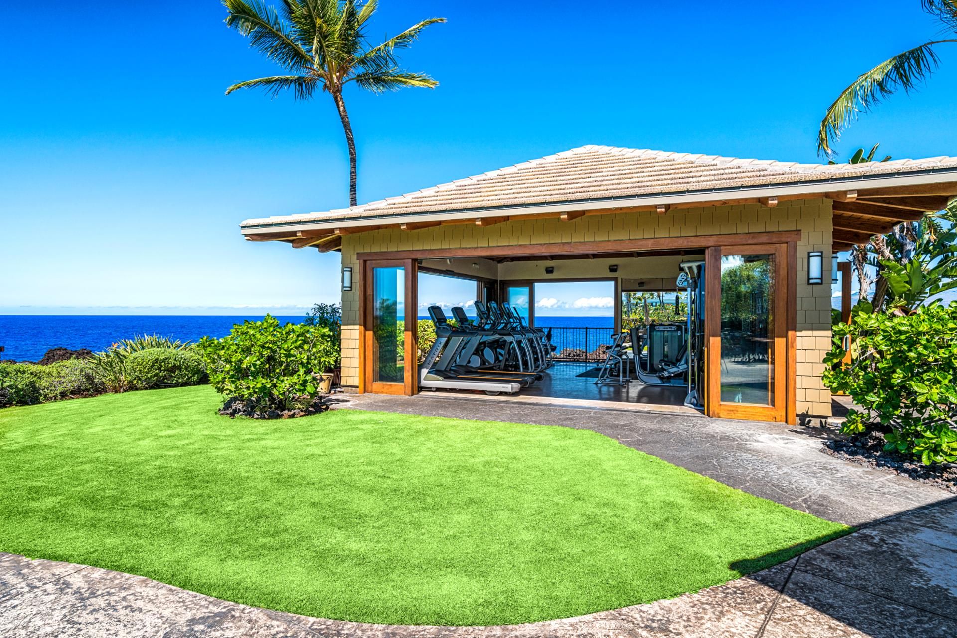 A covered outdoor gym with exercise equipment, overlooking a beach with a clear view of the ocean.