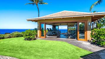 A covered outdoor gym with exercise equipment, overlooking a beach with a clear view of the ocean.