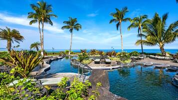 A pool area with palm trees and a view of the ocean.