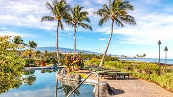 A pool area with lounge chairs, palm trees, and a view of the ocean.