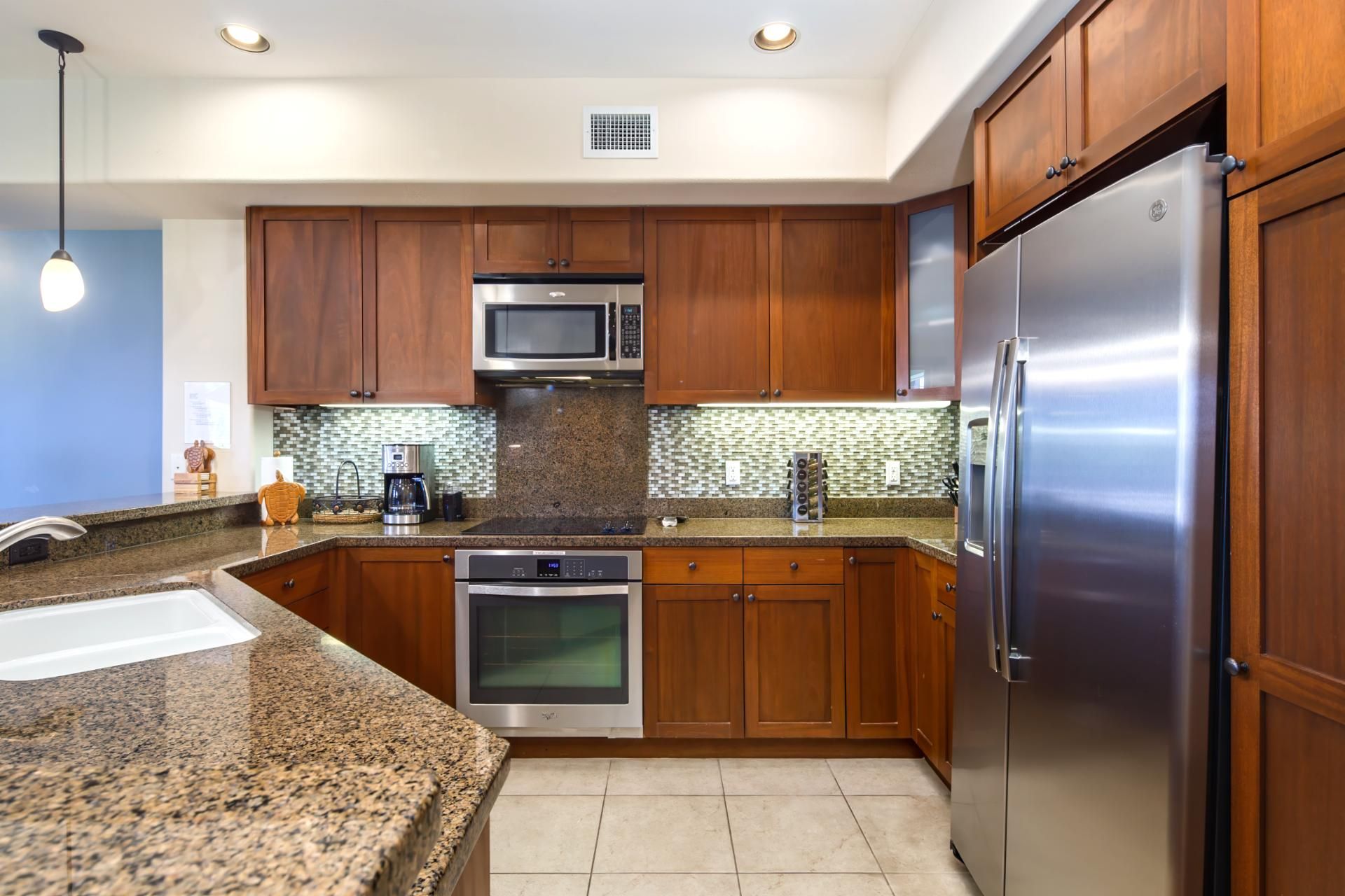 A modern kitchen with wooden cabinets, stainless steel appliances, a granite countertop, and a tiled backsplash.