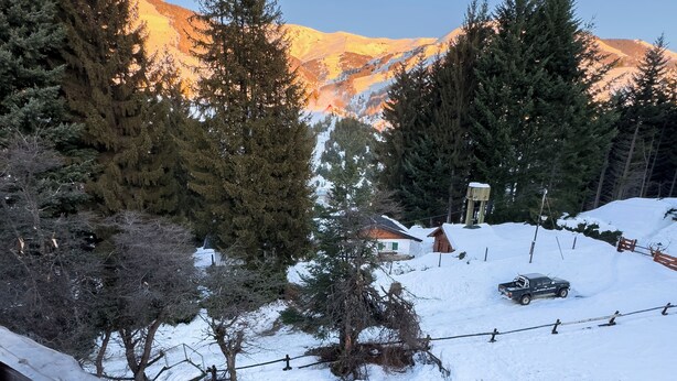 Un paysage enneigé avec une montagne en arrière-plan, une clôture en bois et un véhicule garé dans la neige.