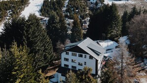 Un bâtiment moderne doté d’un toit plat, entouré de montagnes enneigées et d’une forêt dense.
