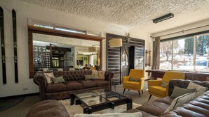 Un salon avec un canapé en cuir marron, une table basse en verre et des fauteuils jaunes. On y trouve un grand miroir et une cheminée.