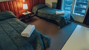 Une chambre d’hôtel avec deux lits, une petite table, une lampe et une fenêtre donnant sur des arbres.