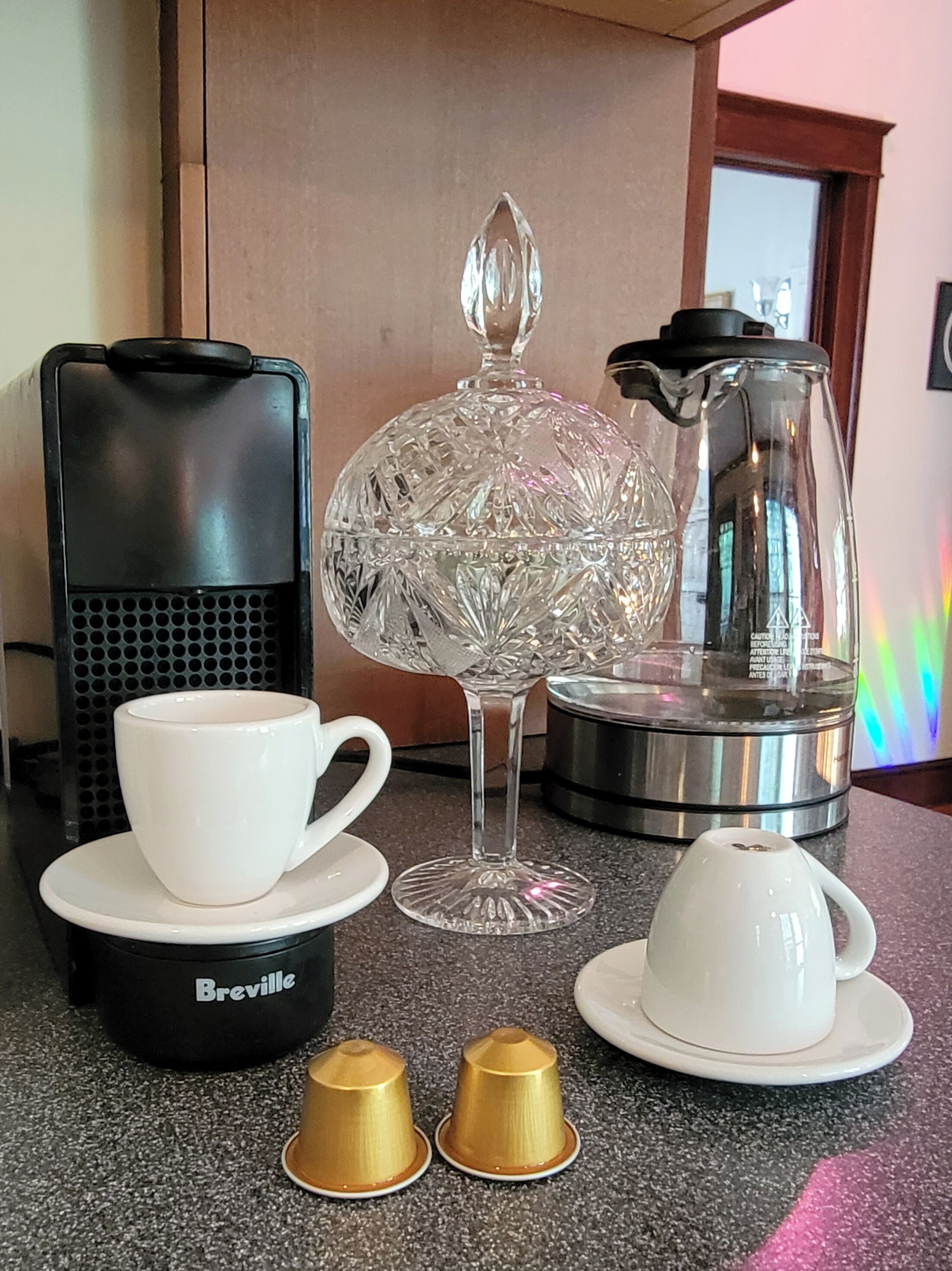 A coffee maker, a glass carafe, a cup, a saucer, and two gold-colored cups on a countertop.