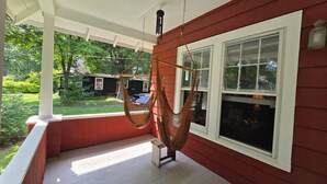 Une véranda avec un hamac et une vue sur une maison et la verdure.