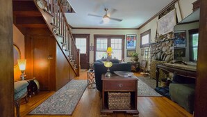 Un salon spacieux avec un escalier en bois, un ventilateur de plafond, une cheminée et un téléviseur.