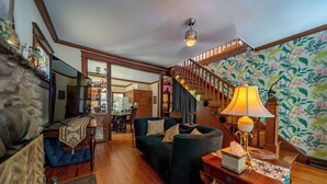 Un salon chaleureux avec un escalier, un plancher en bois et un papier peint à motifs floraux.